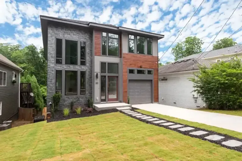 Modern two-story house with large windows, gray and brick facade, and a manicured lawn