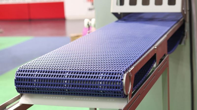In un contesto industriale o produttivo, un nastro trasportatore modulare in plastica blu scorre lungo un telaio metallico.
