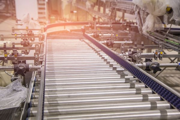 Sistema di nastri trasportatori industriali con rulli metallici e sponde laterali in uno stabilimento di produzione.