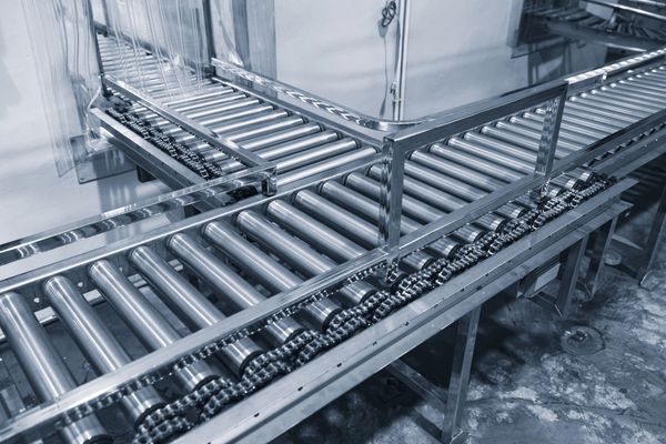 Un sistema di nastri trasportatori metallici con rulli e meccanismo di trasmissione a catena in un contesto industriale.