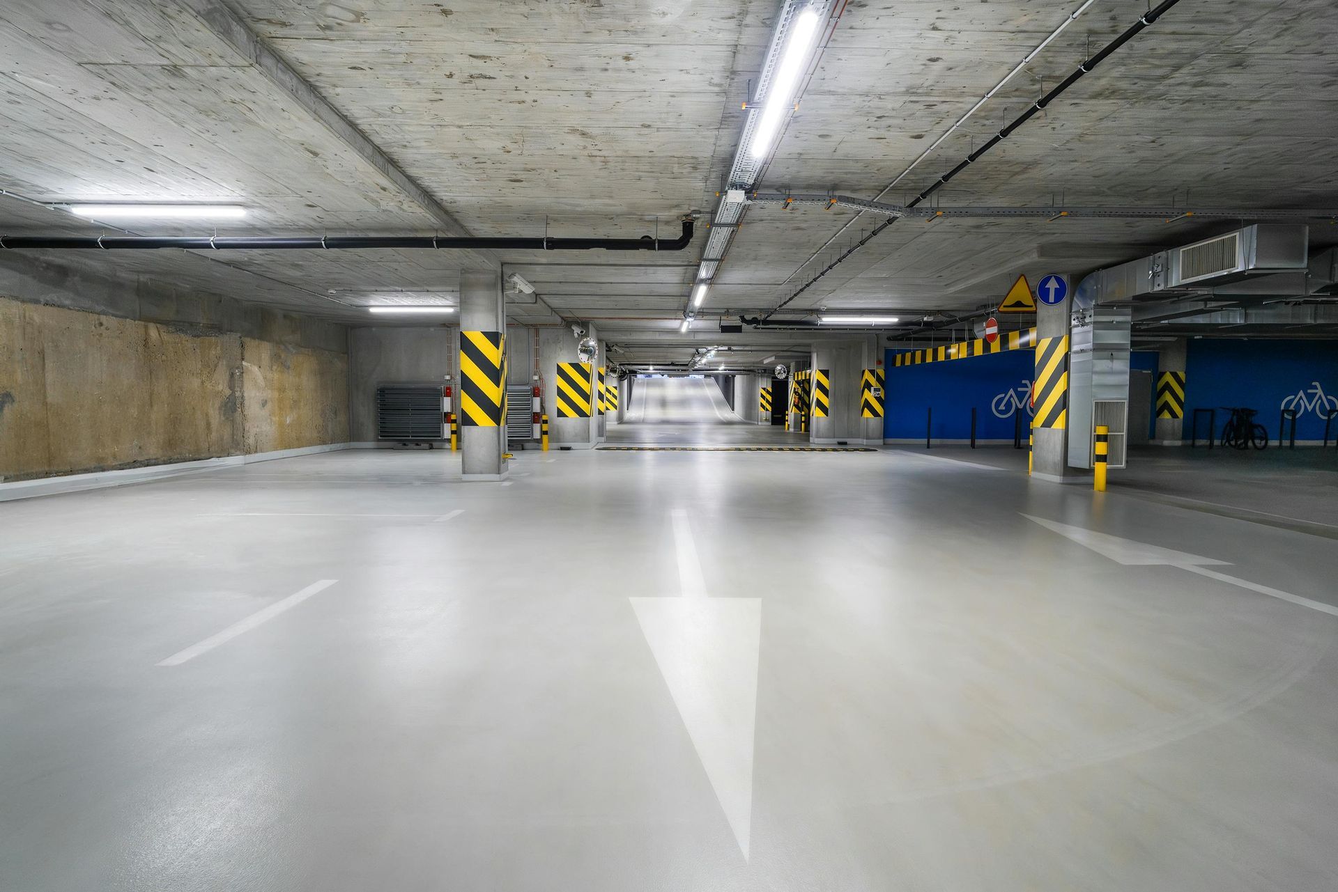 Empty, well-lit parking garage with painted arrow, support columns, and overhead lights.