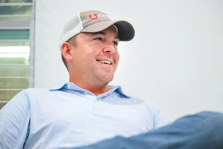 A man wearing a hat and a blue shirt is sitting on a couch.