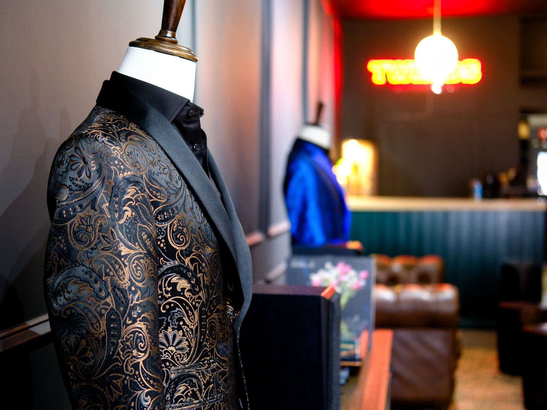 Mannequin in a patterned suit jacket, black collar. Interior shot with blurred background, showcasing clothing store.