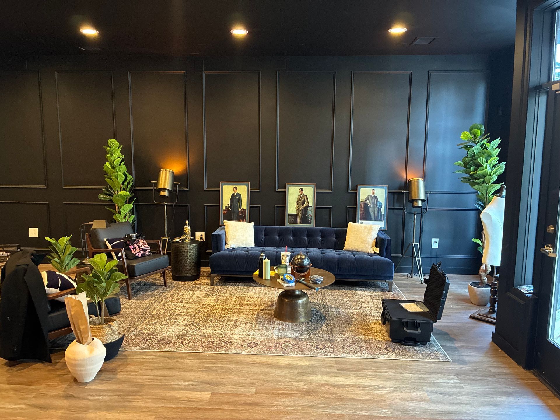 Living room with black paneled walls, blue velvet sofa, decorative rug, and plants.