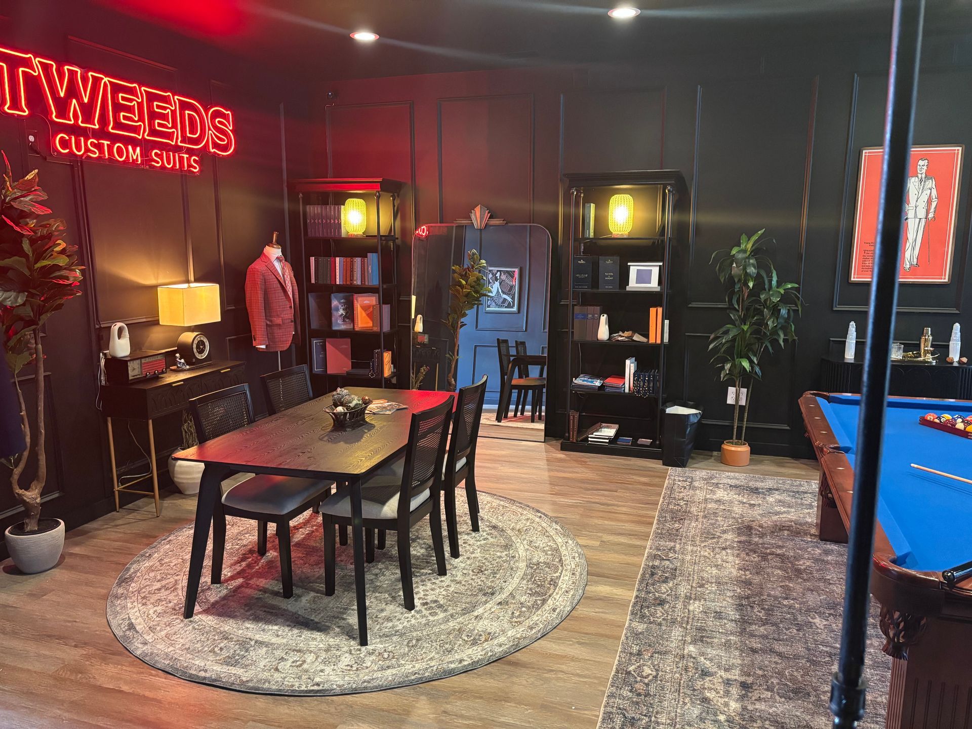 Room with a dining table, pool table, bookshelves, and neon sign that reads