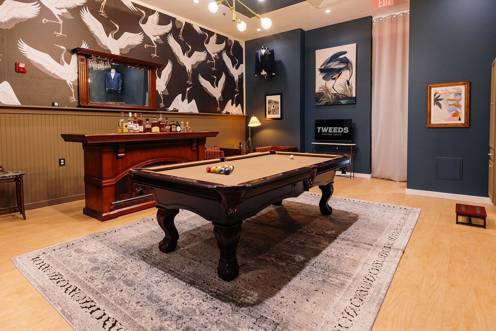 A dimly lit game room with a pool table, bar, and abstract wall art; blue and brown tones.