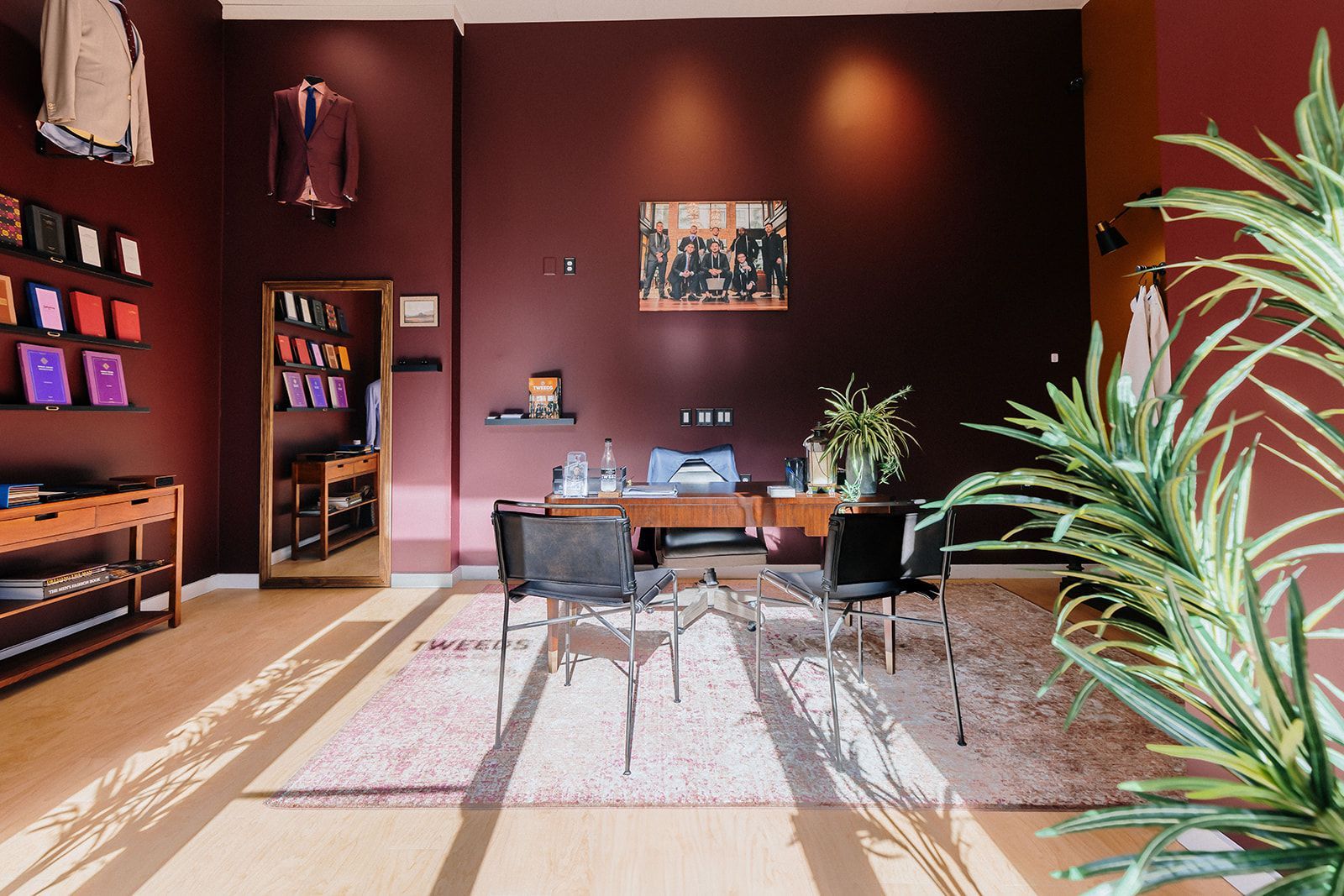 Interior of a clothing store with a burgundy wall, a desk with chairs, and suits on display.