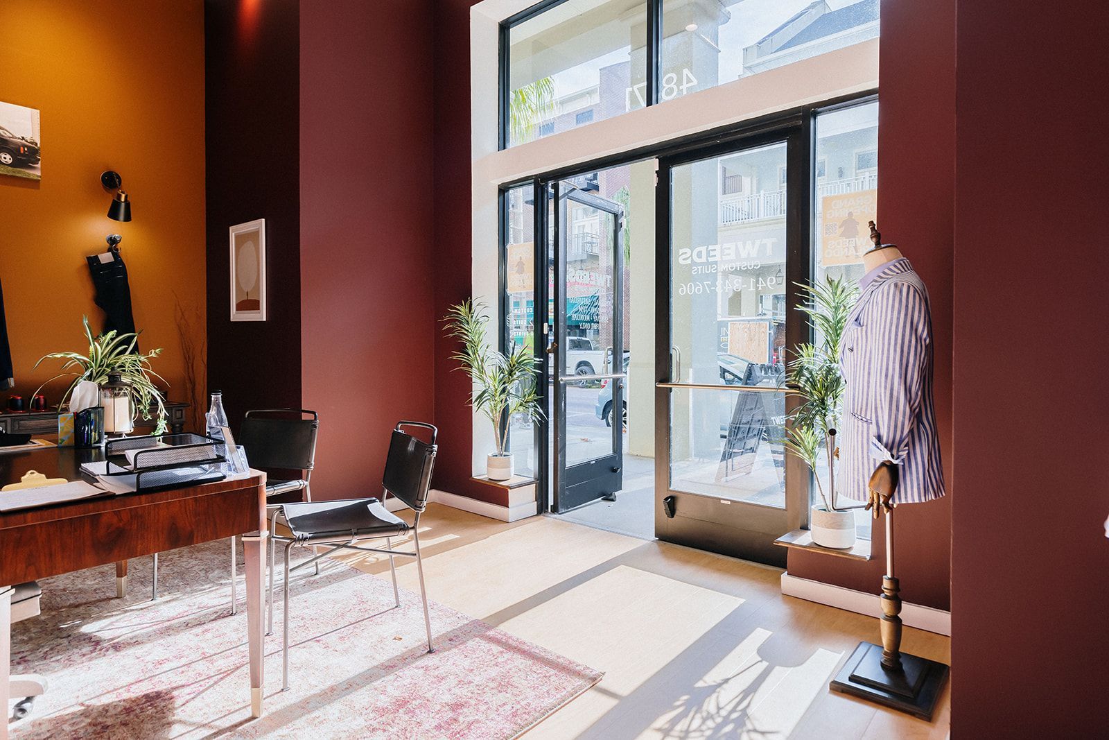 Storefront interior with glass doors, maroon walls, wooden desk, and a dress form.