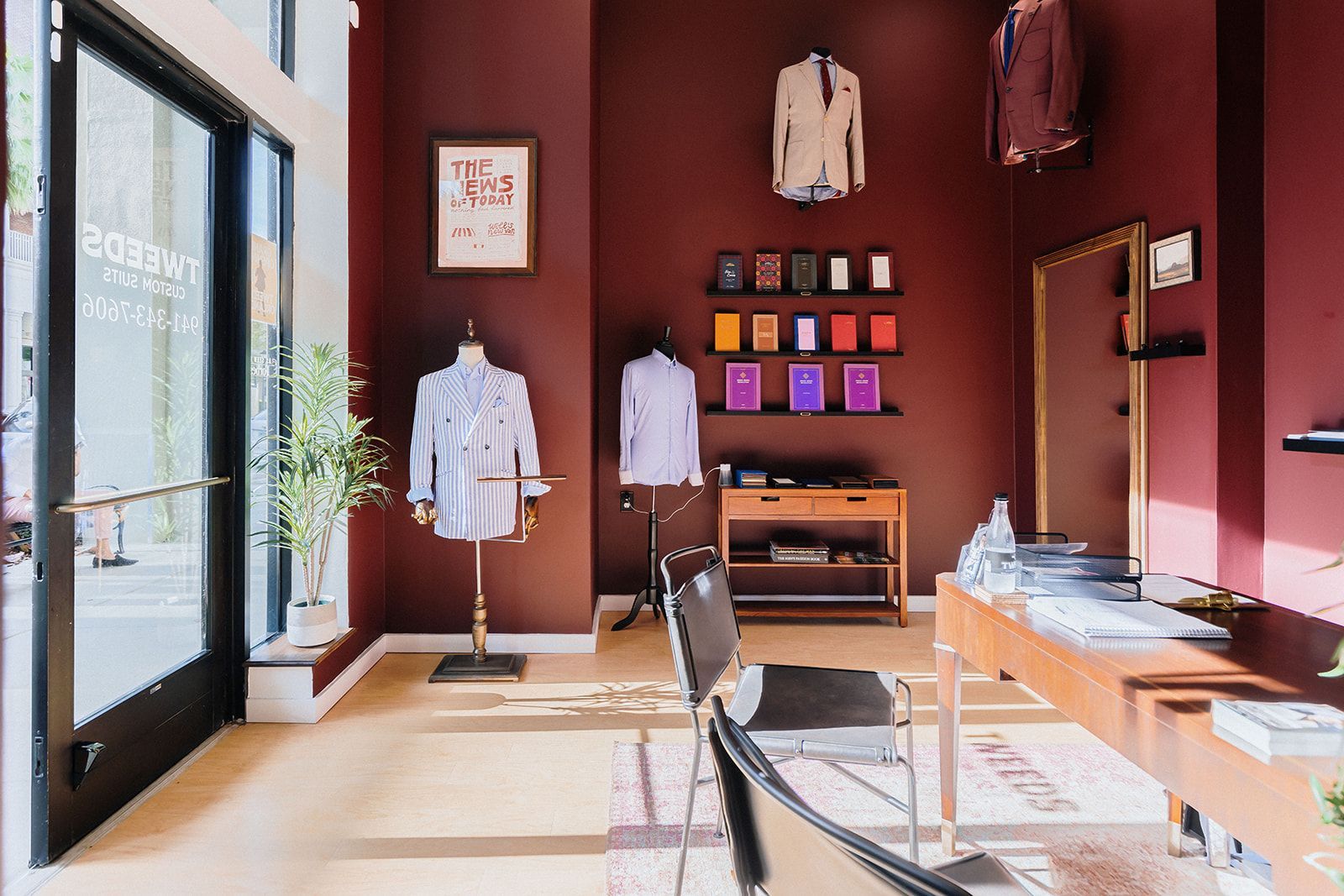 Interior of a tailored clothing shop with suits on display. Burgundy walls, wood floor, and suits on mannequins and hangers.