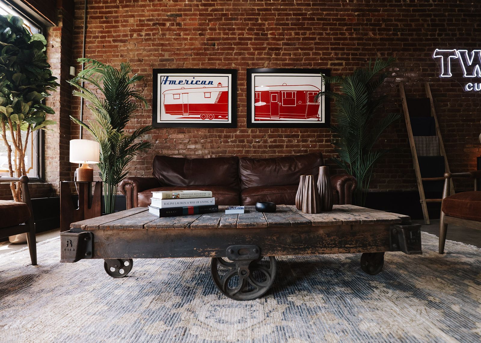 Rustic living room: Leather sofa, wooden coffee table with wheels, brick wall, artwork, plants.
