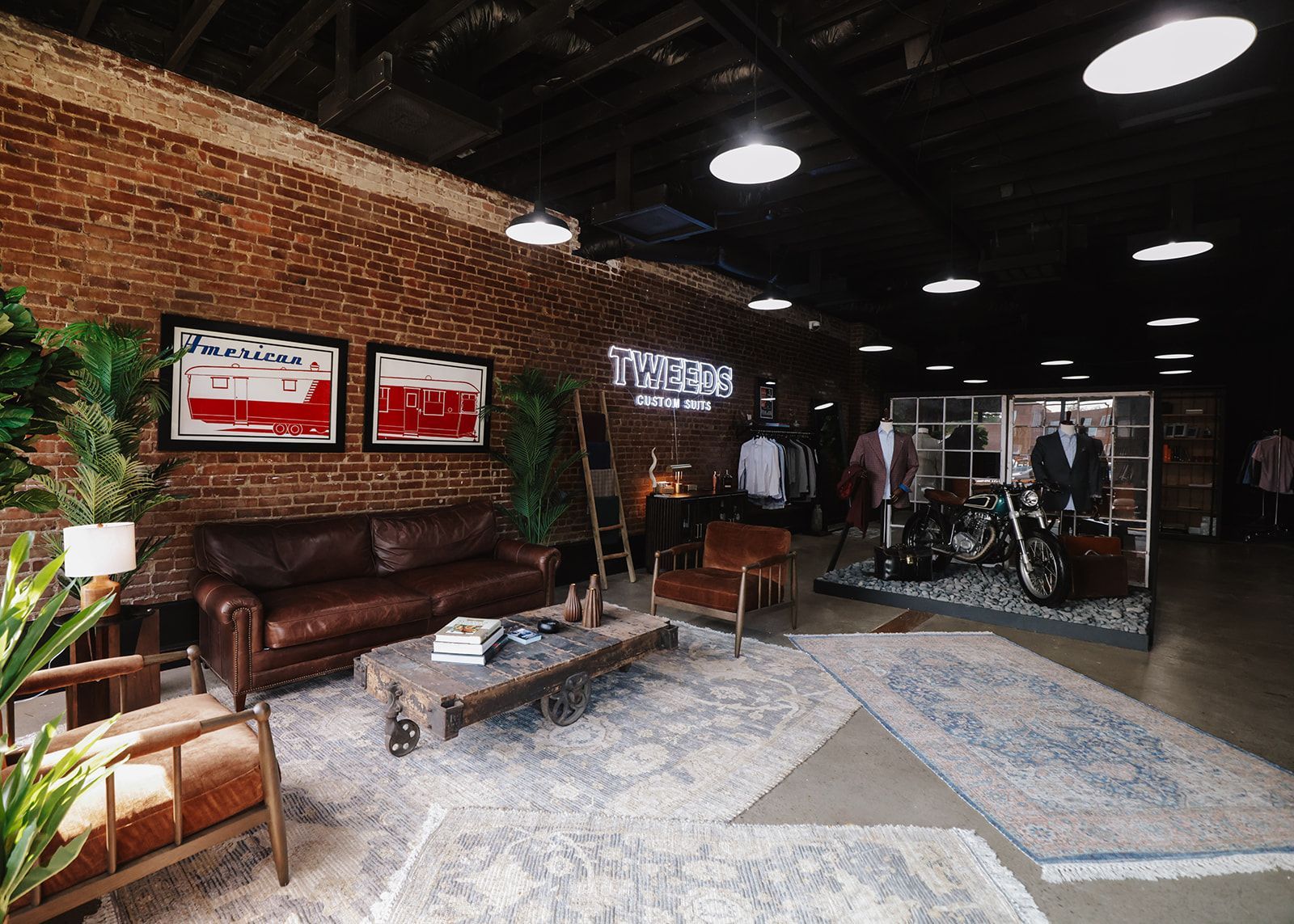 Interior of a store with a seating area, merchandise display, and a motorcycle. Brick walls, rugs, and overhead lighting.