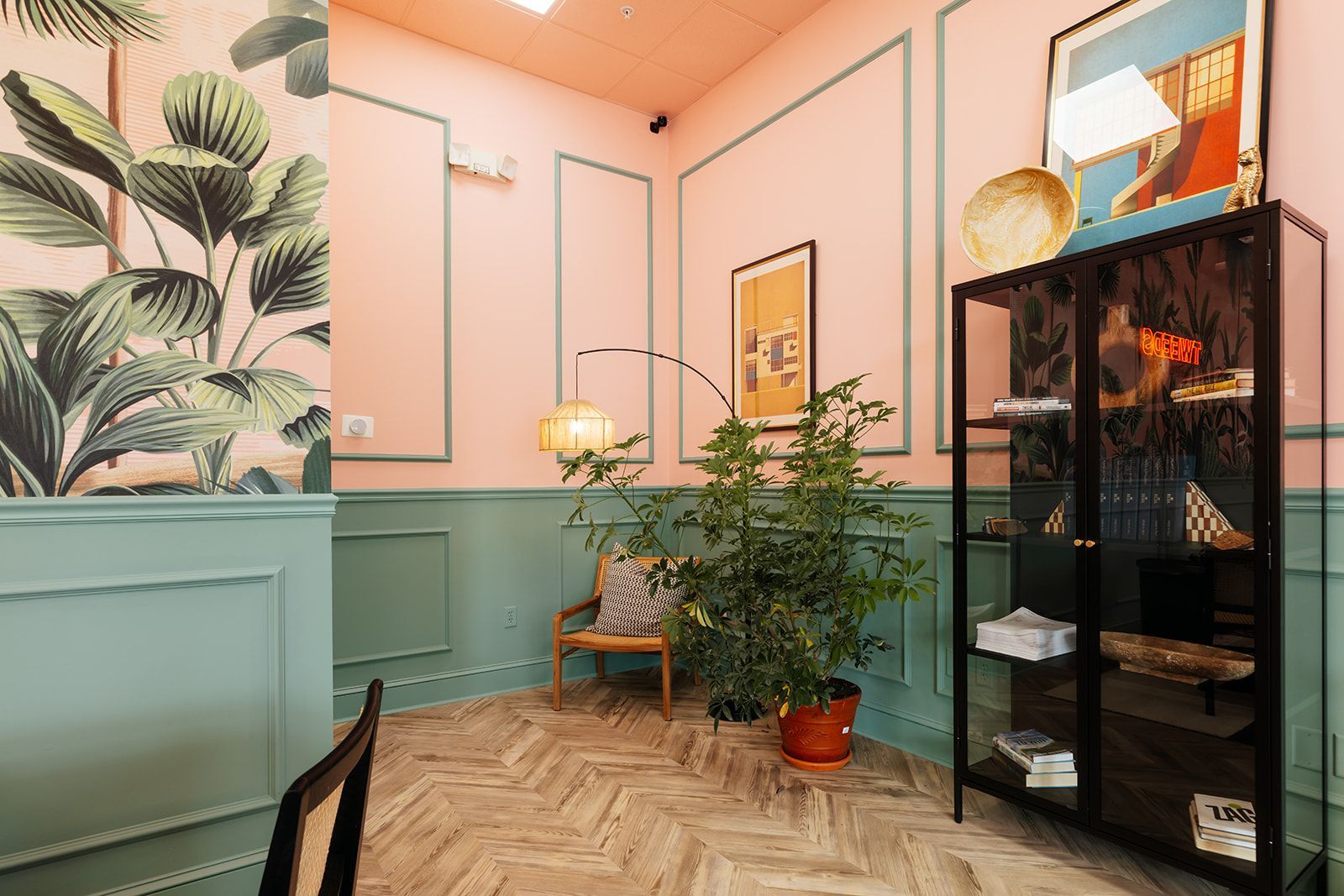 Interior of a room with pink and green walls, patterned floor, and plants. A display case is on the right.