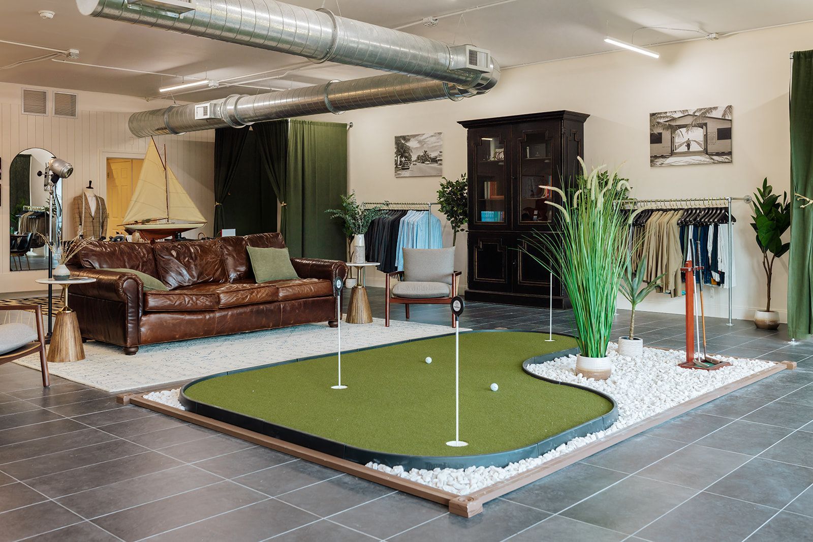 Indoor golf green in a custom suit clothing store, brown leather sofa, clothing racks, and decorative plants.