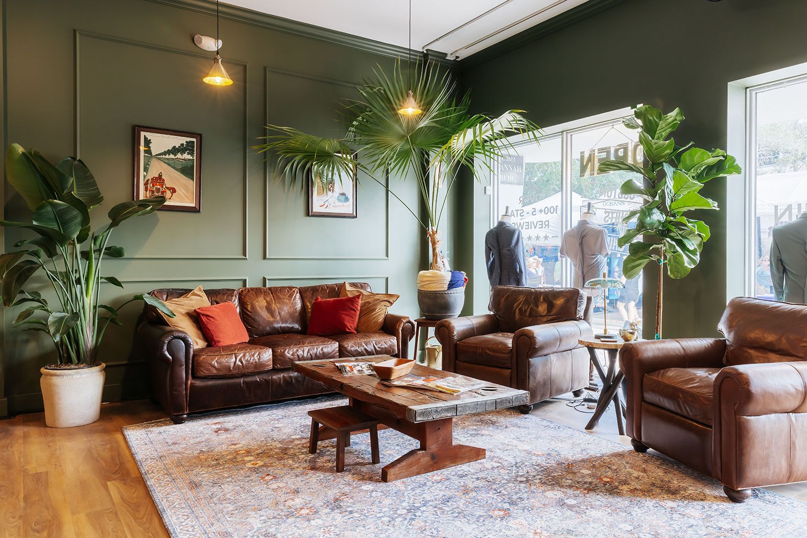 Living room-like area in a retail store with brown leather furniture, green walls, plants, and an