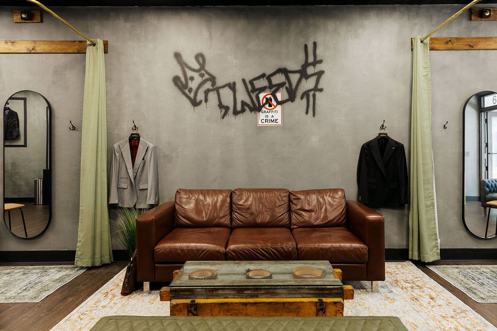 Interior of a custom suit clothing store with a leather sofa, two hanging jackets, graffiti art, and mirrors.