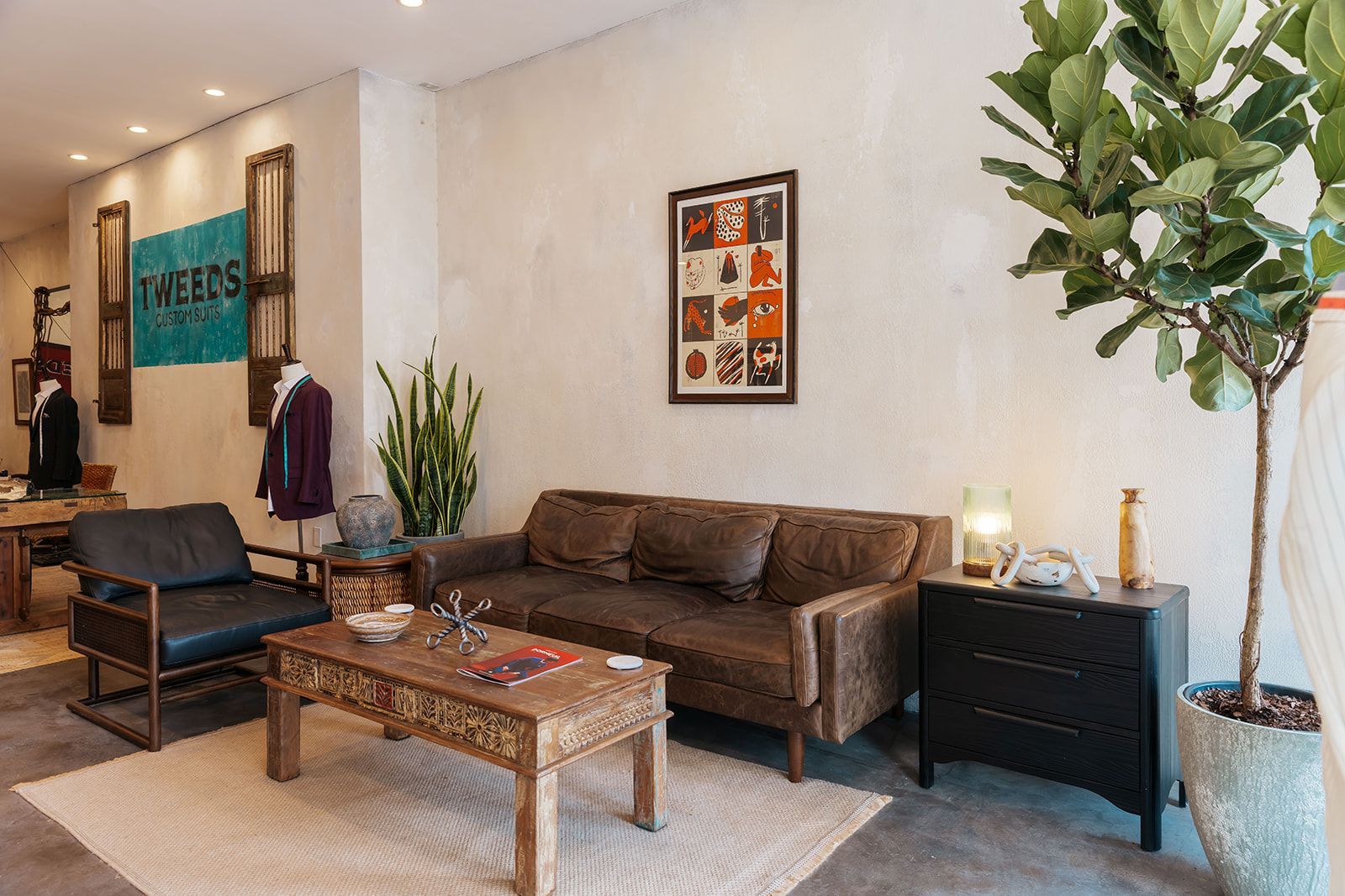 Cozy shop interior with brown leather couch, black chair, wooden table, and potted plants.