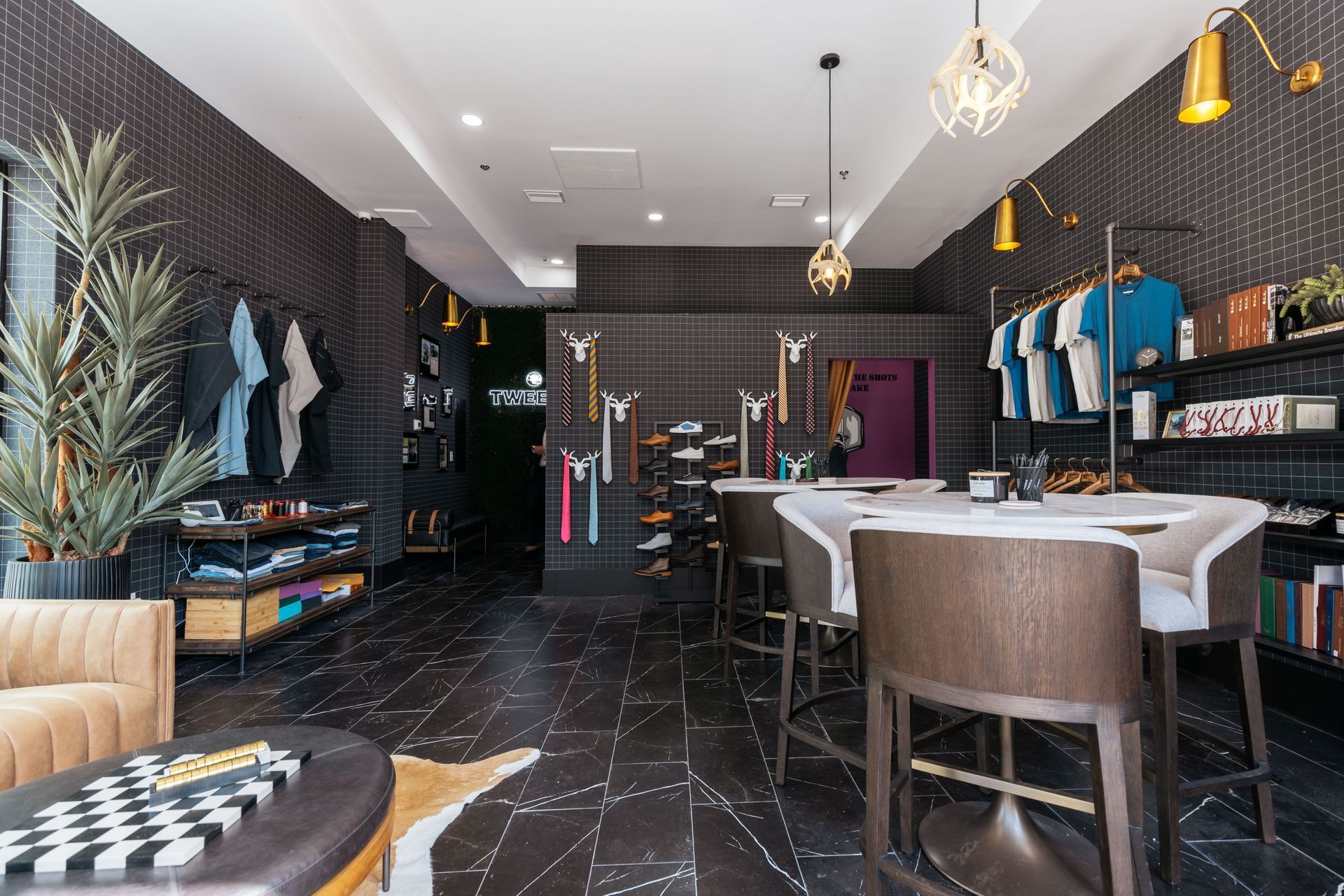 Clothing store interior with clothing racks, seating, and decorative lighting; dark colors.