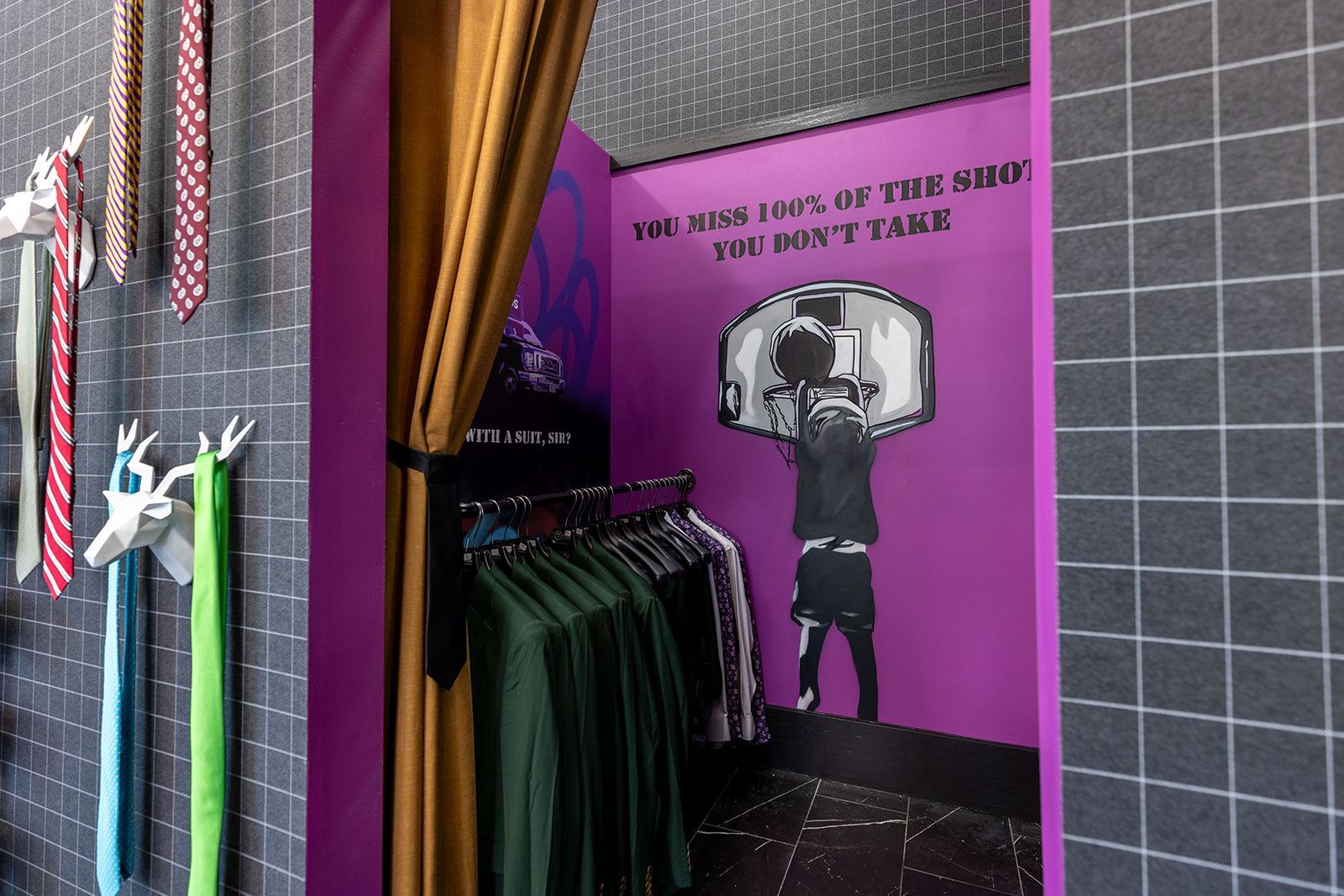 Clothing store interior with ties, clothes racks, purple wall with basketball art, and yellow curtain.