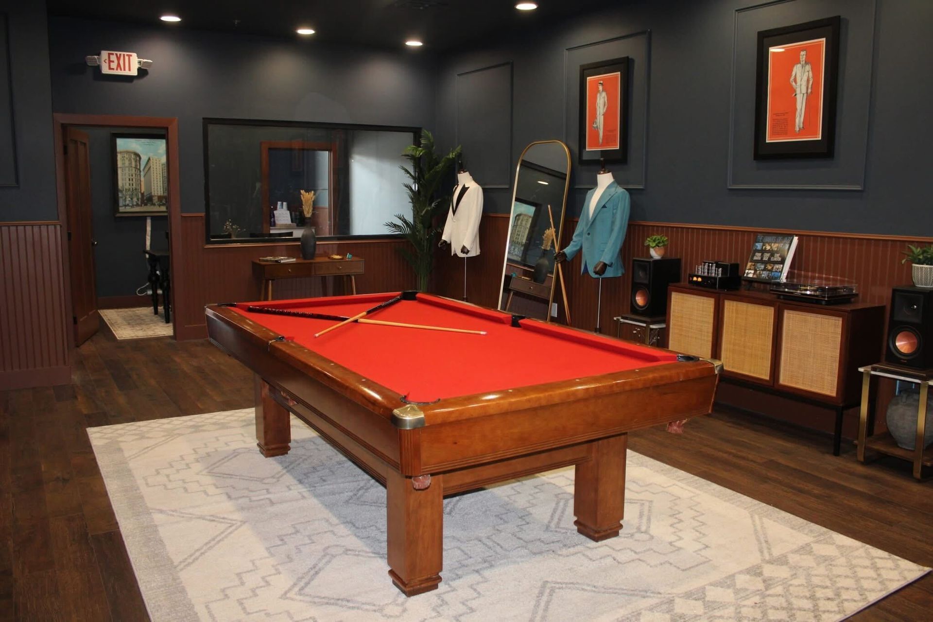 Pool table in a room with a red felt surface, dark walls, and suit display.