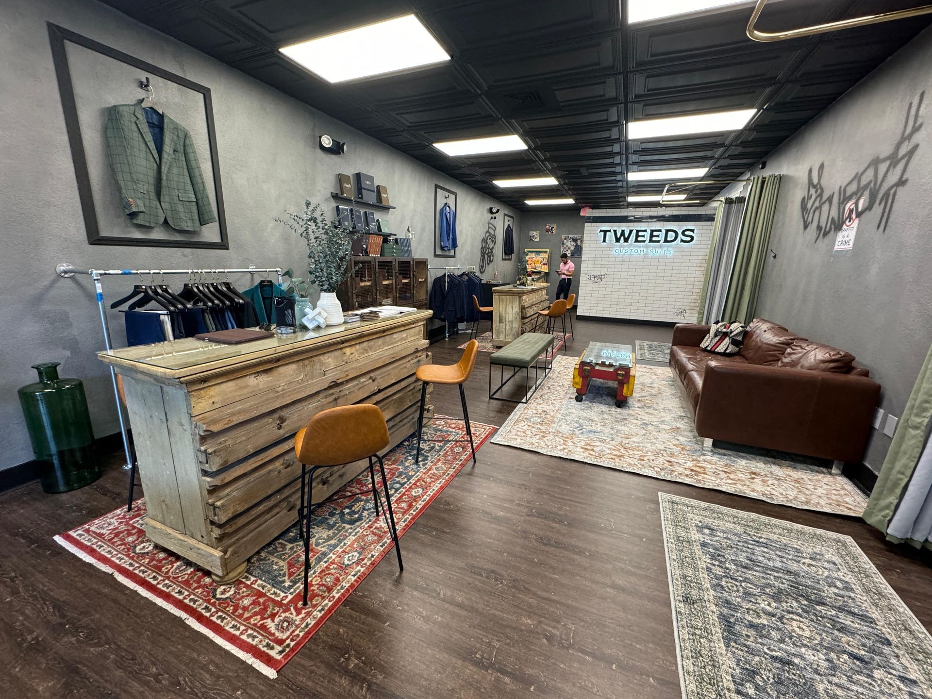 Interior of a men's clothing store with tweed jackets, a rustic counter, and rugs.