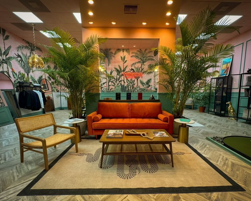 Living room with orange sofa, wooden furniture, plants, and a floral mural.