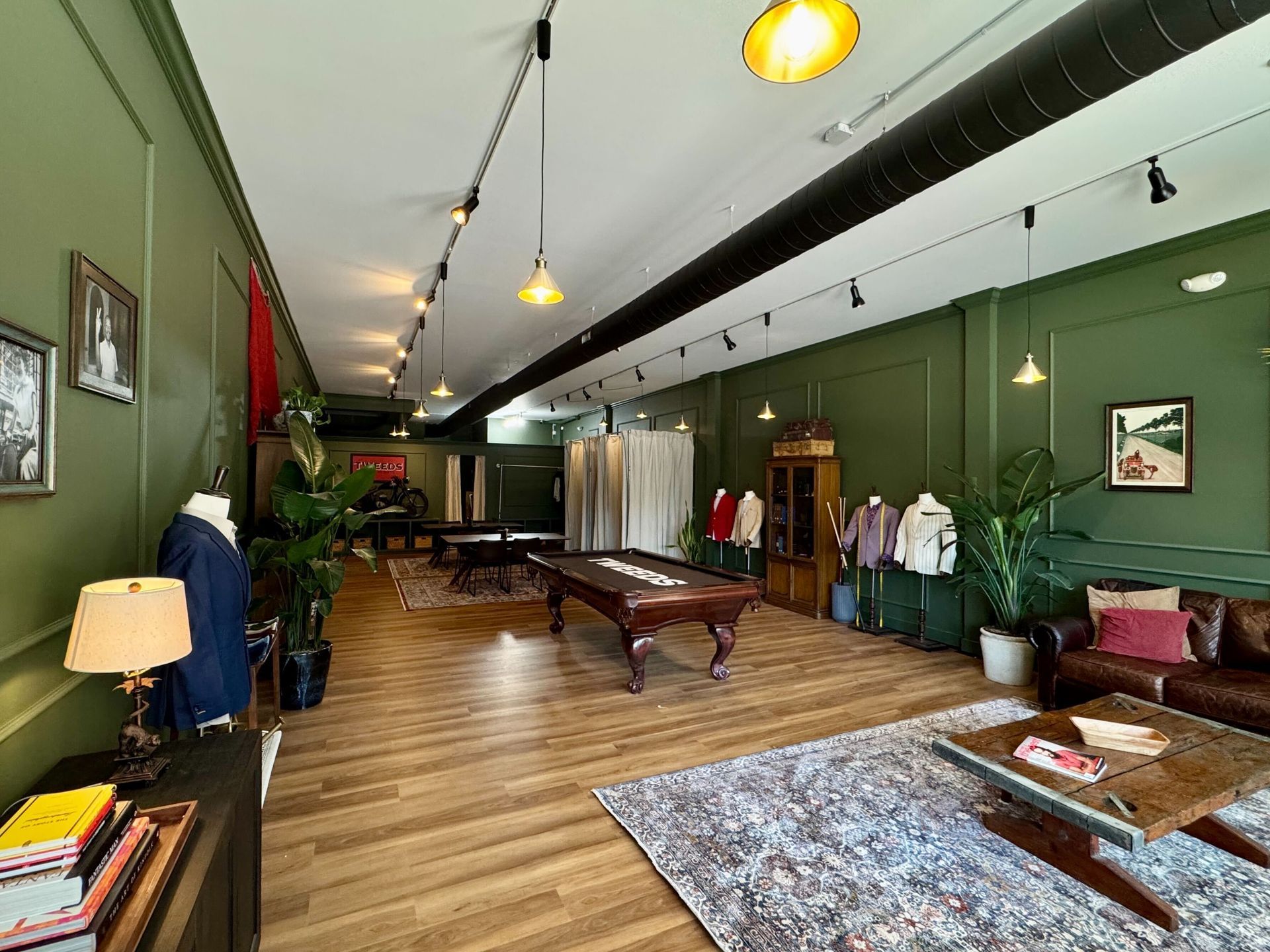 Green-walled room with pool table, seating area, clothing displays. Track lighting illuminates the space.