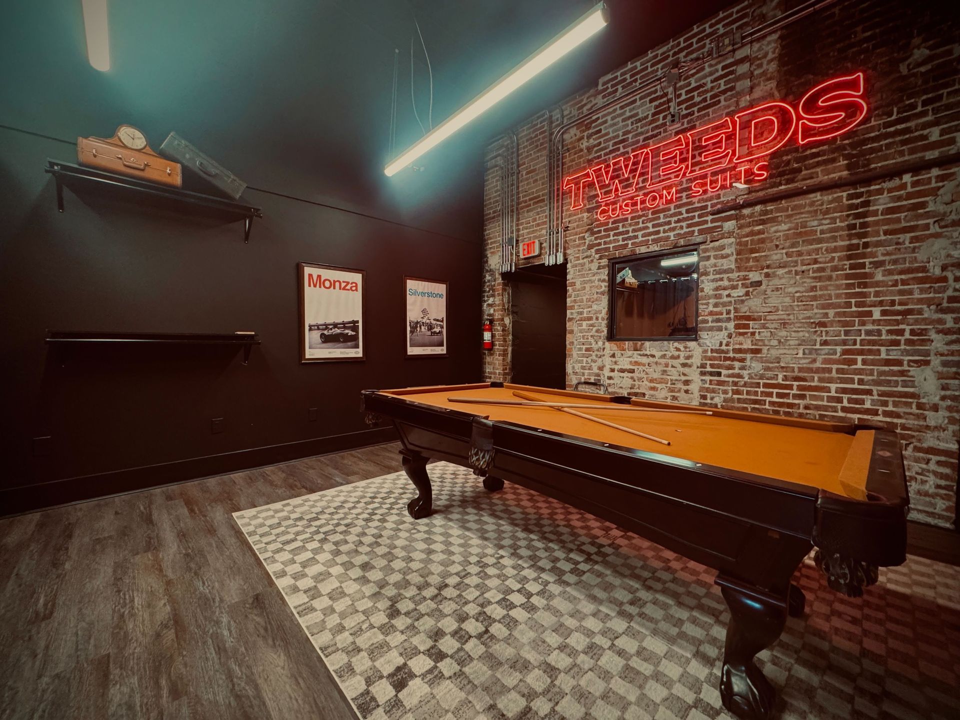 A pool table in a dimly lit room with exposed brick and a neon sign.