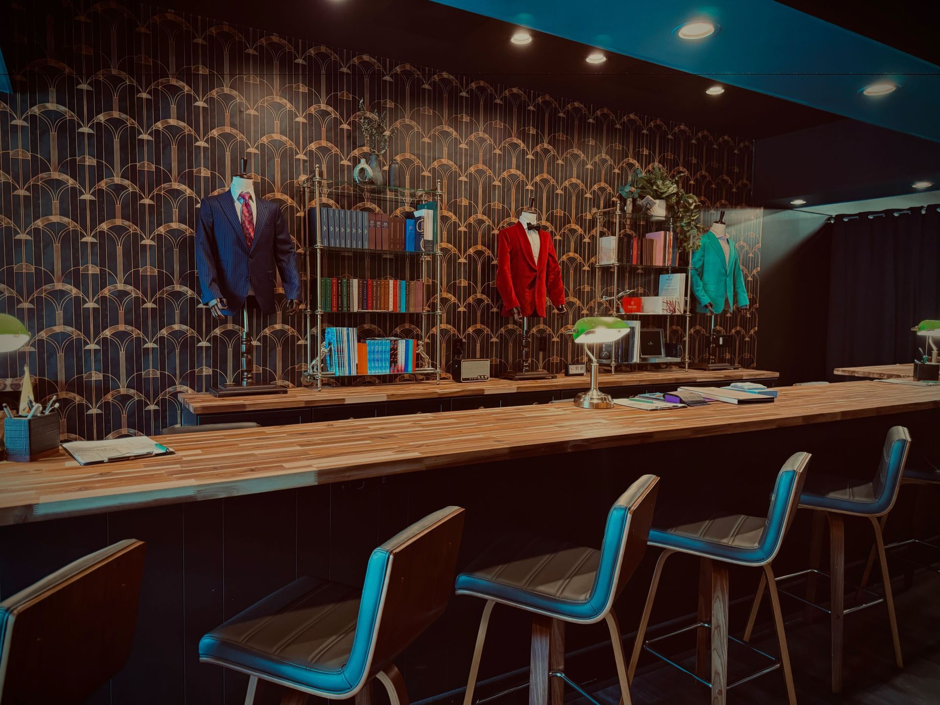 Bar with stools and suits hanging on a patterned wall, with books on shelves.