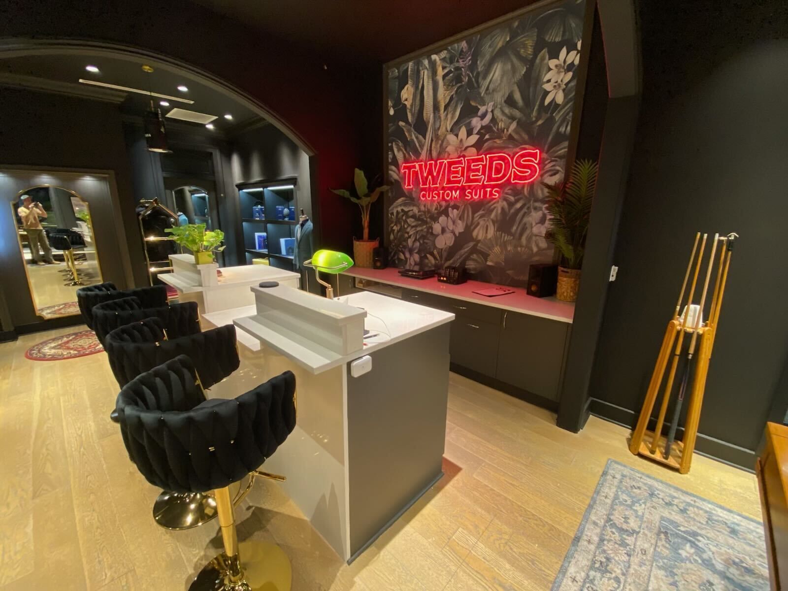Reception area of a salon, black chairs with gold bases, light wood floor, gray counter.