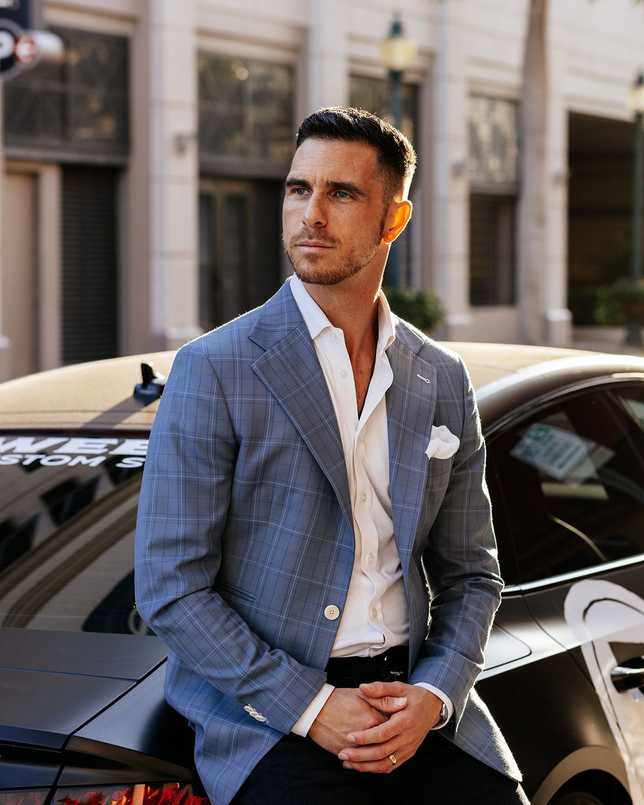 A man in a suit is sitting on the back of a car.