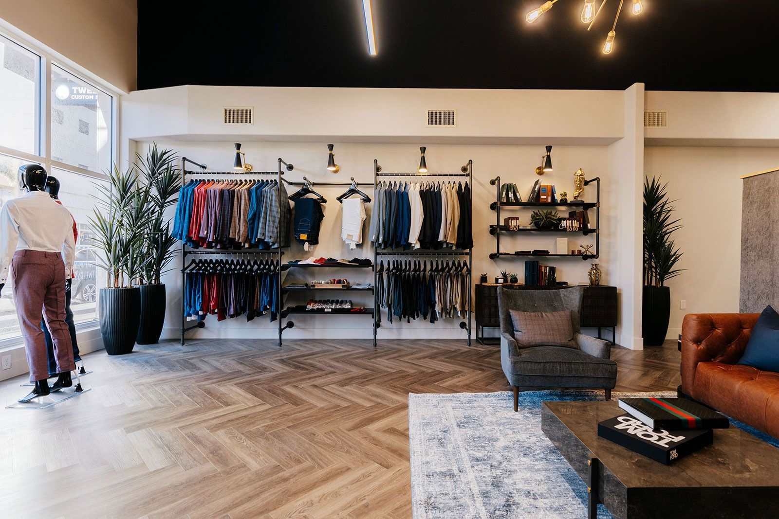 Clothing store interior with racks of clothes, a seating area, and large windows.