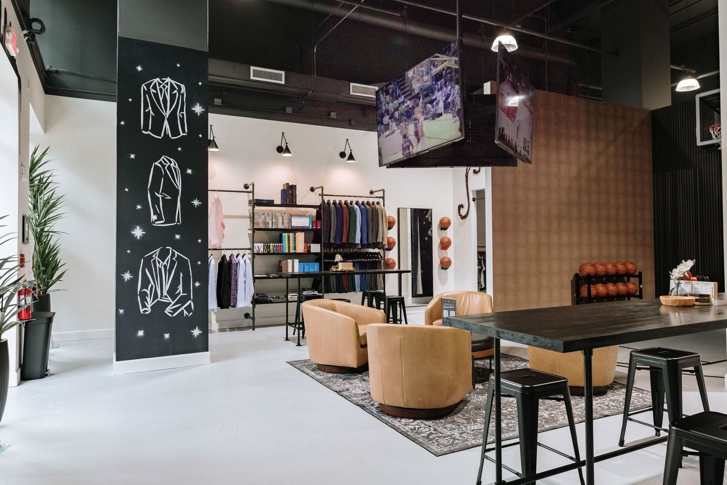 Interior shot of a modern clothing store with seating, displays, and a TV. Black and white decor with light-colored seating.