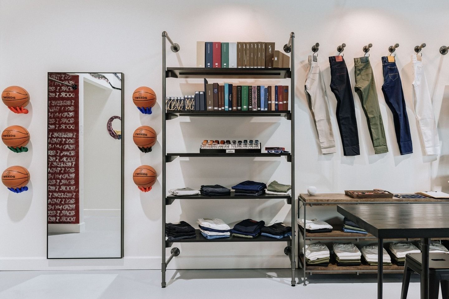 Clothing store interior with shelving, hanging jeans, basketball art, and a large mirror.