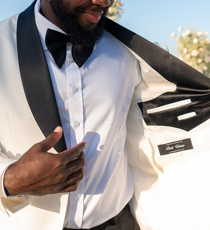 Man in a white tuxedo with black lapels adjusting his jacket, showing the inside pocket.