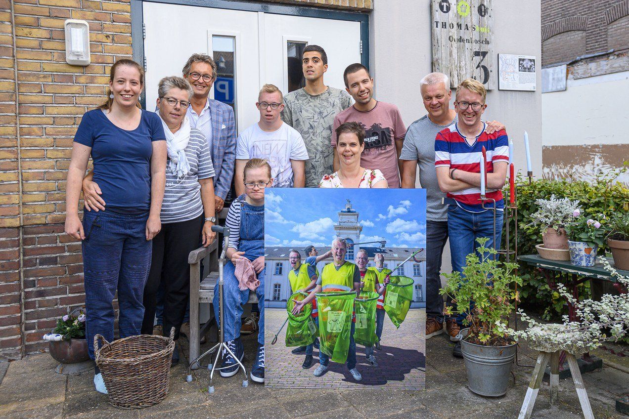 Een groep mensen staat voor een gebouw en houdt een schilderij vast.