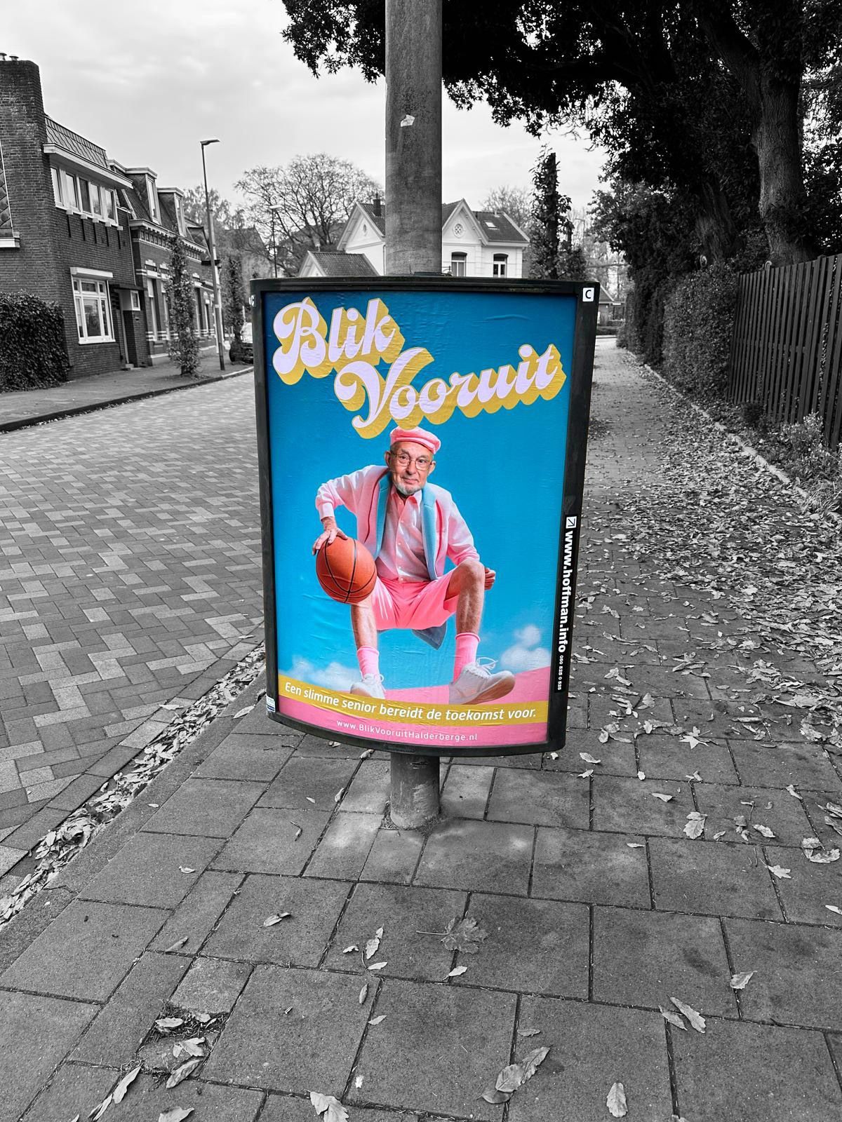 Een felblauwe poster, bevestigd aan een paal in een straat, toont een persoon in roze kleding die een basketbal vasthoudt.
