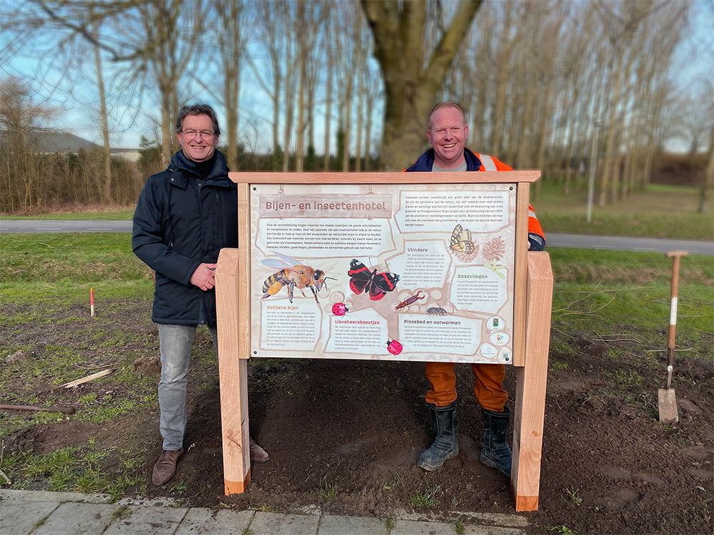 Twee mannen staan naast een houten bord.