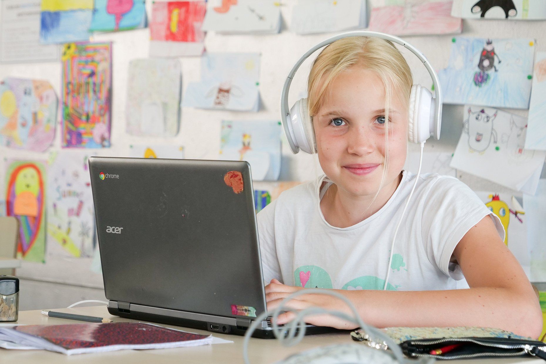 Een jong meisje met een koptelefoon zit achter een laptop.