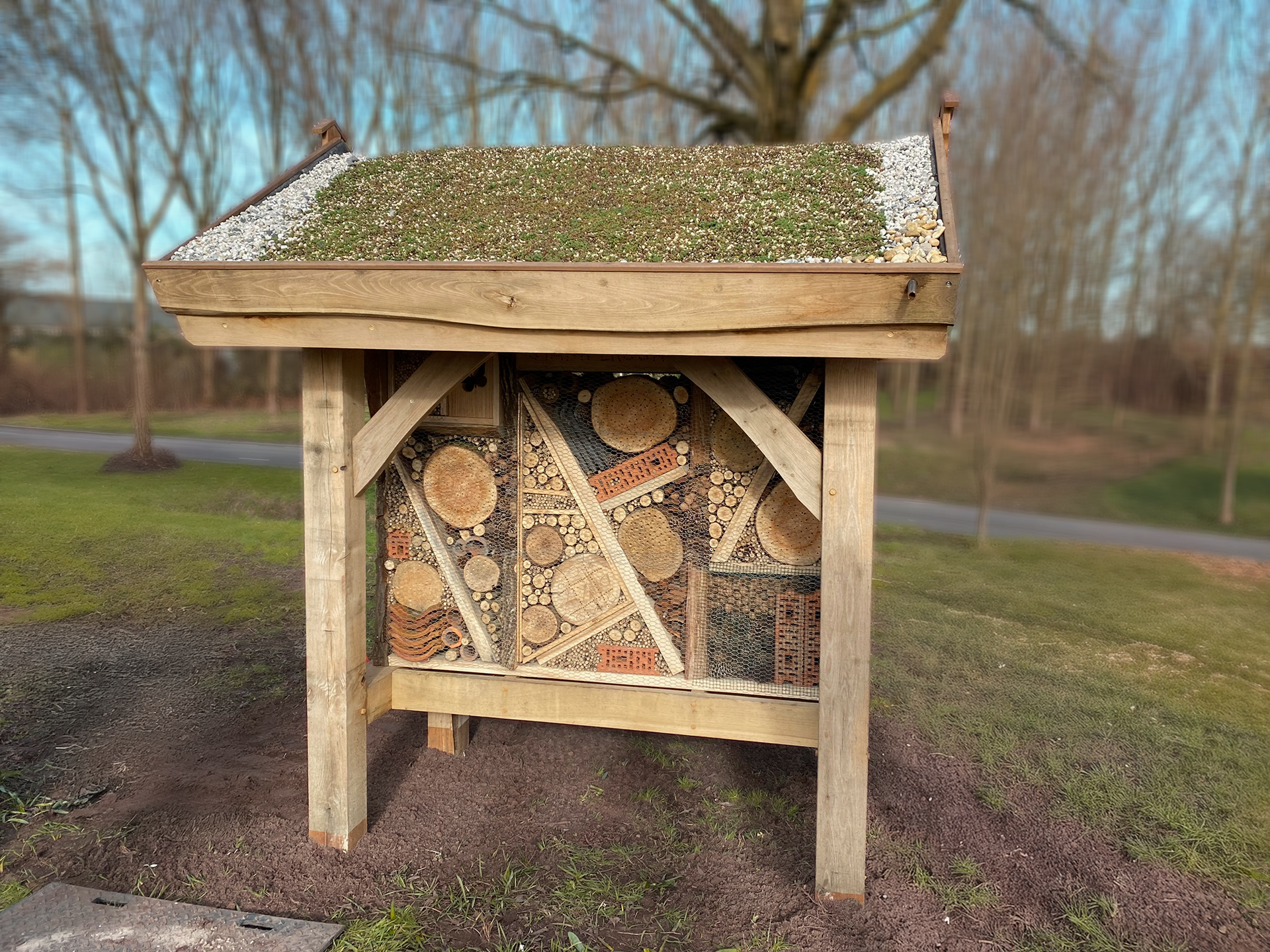 Een houten constructie met een groen dak staat midden in een veld.