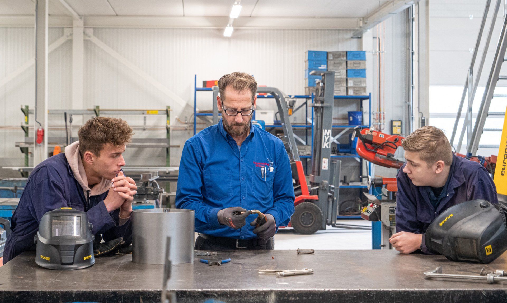 Drie mannen zitten aan een tafel in een fabriek en praten met elkaar.