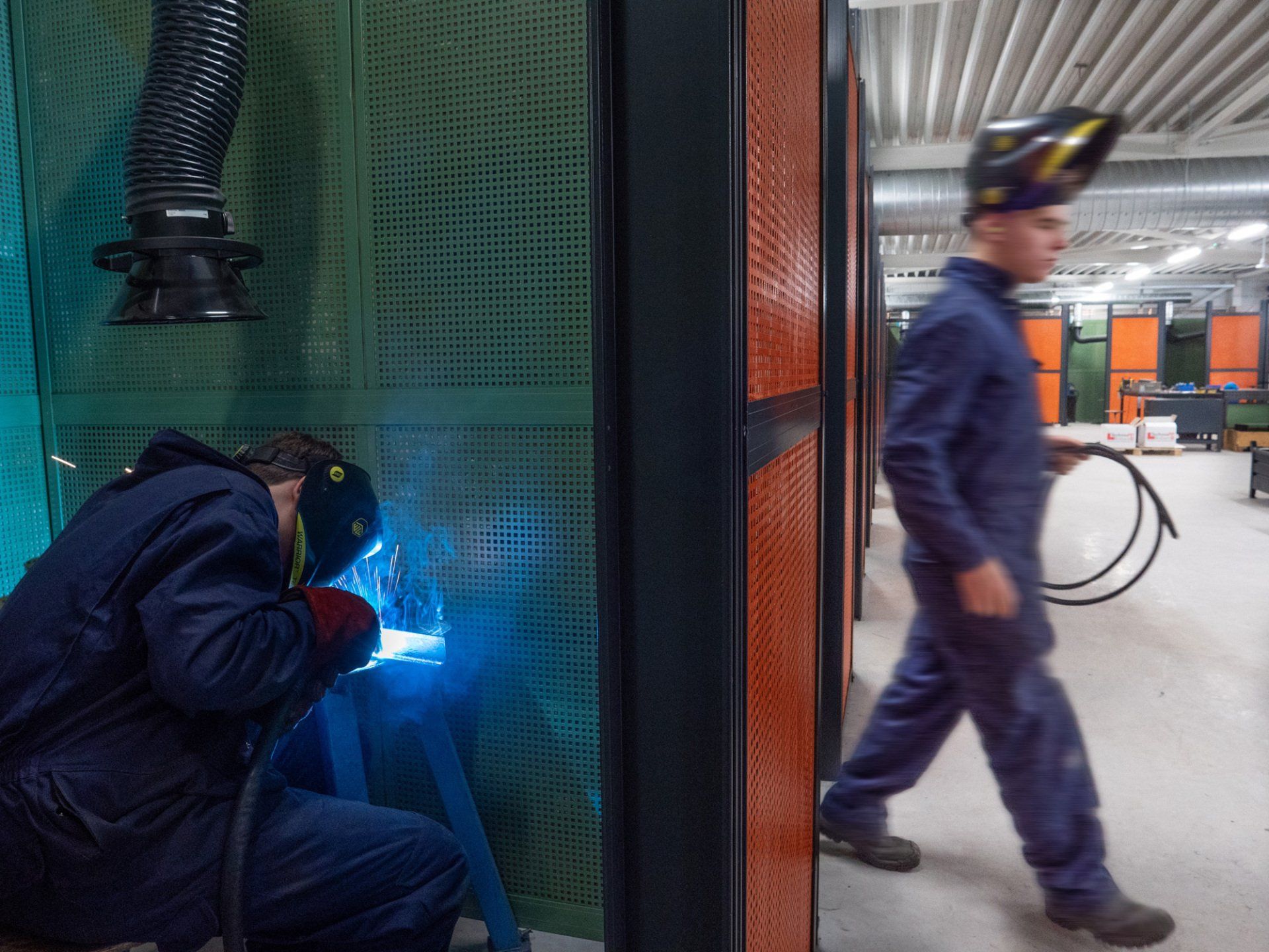 Een man is aan het lassen terwijl een andere man voorbij loopt