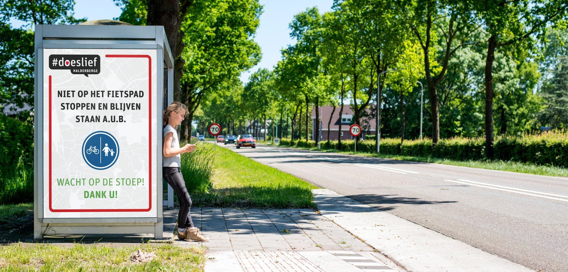 Een vrouw staat bij een bushalte en kijkt op haar telefoon.