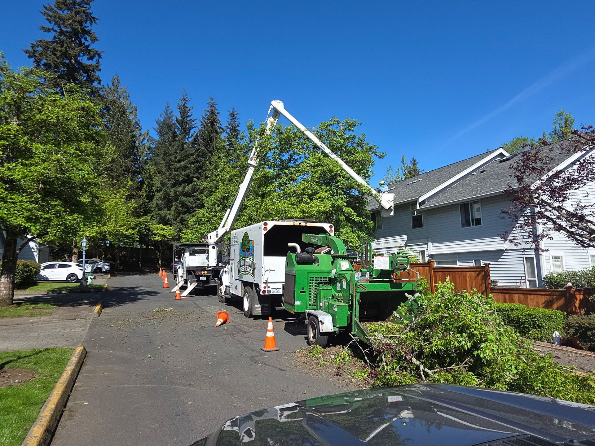 Utility truck with raised boom parked on a suburban street beside a house and cones