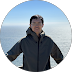 Person in a dark jacket standing outdoors against a snowy mountain backdrop.
