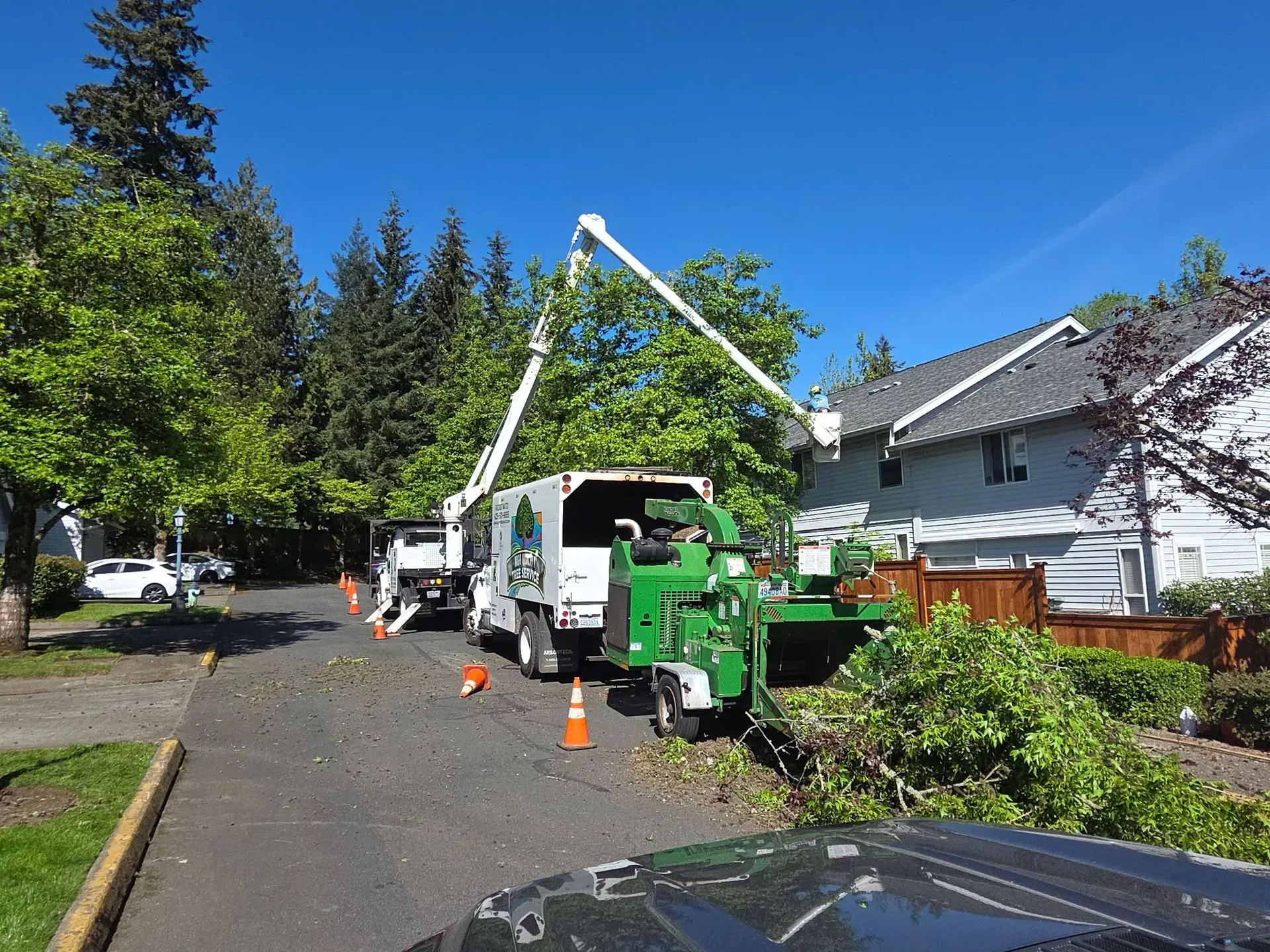 Utility truck with boom lift and orange cones on a suburban street beside houses and trees