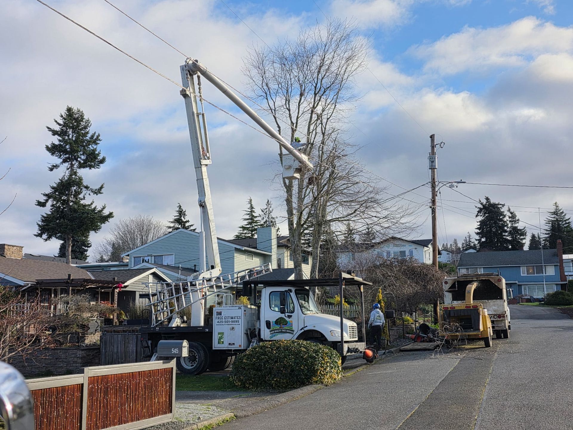 Utility trucks and workers repairing power lines on a residential street after storm damage.