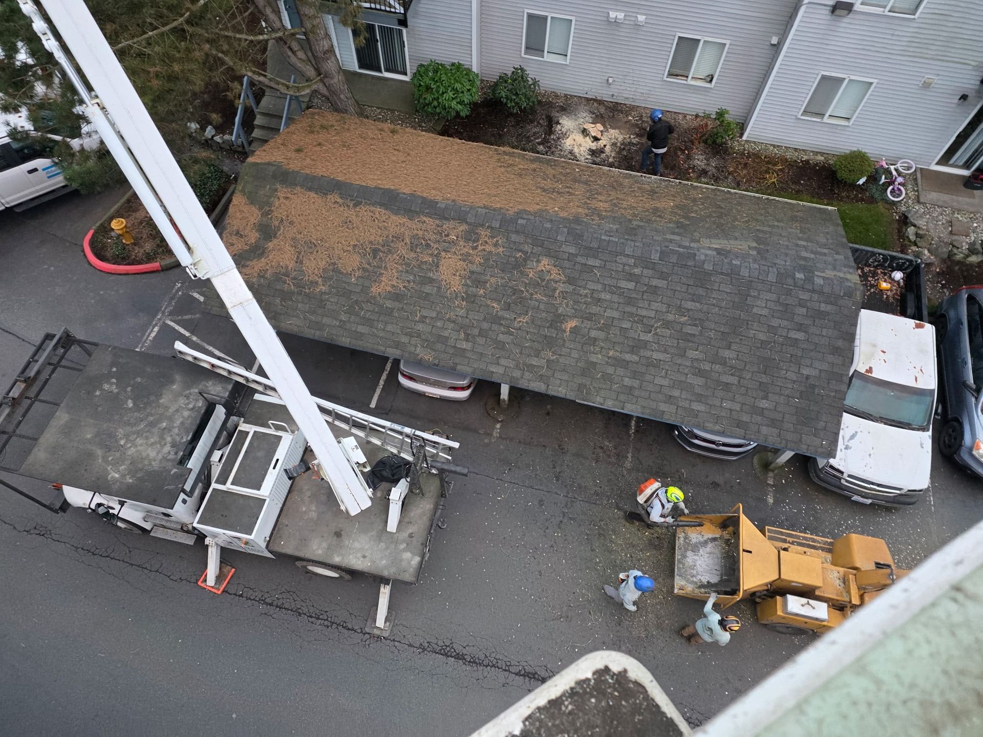 Aerial view of a roof replacement with workers, shingles, and equipment beside a house and truck.