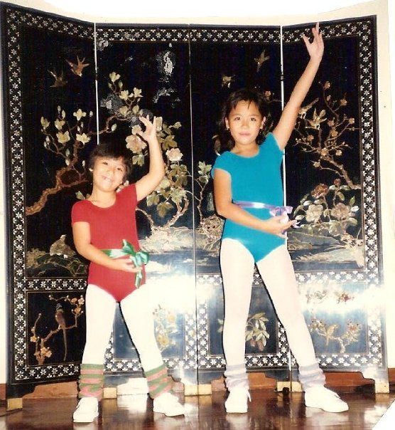 Two children in leotards and tights, posing in front of a black screen with floral patterns.