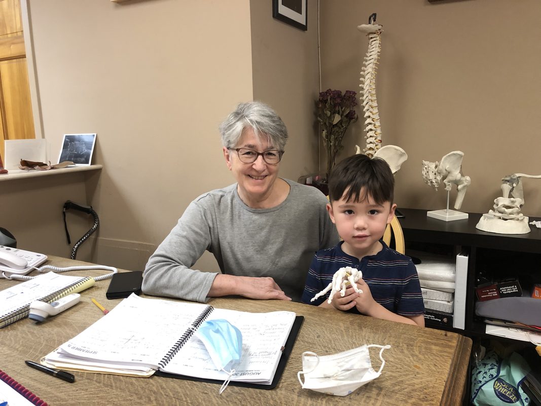 Woman and child at desk. They sit near a computer, papers, and a mask in a medical office.