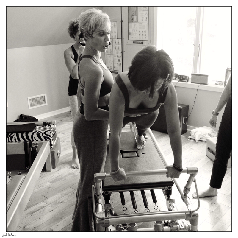 Woman on Pilates reformer, guided by an instructor in a studio setting.